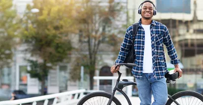 Smiling young man wearing headphones and leaning against his bike.