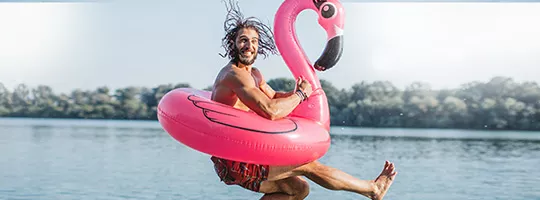 Holiday Discounts - Man jumping into water on holiday with a large pink flamingo float ring